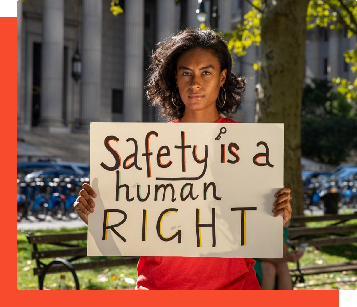 A head-on portrait of a person standing outdoors, holding a white sign with the words 